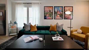 A modern living room with a green sofa, a yellow armchair, a coffee table with a book and a plant, and a cityscape painting on the wall. - Retro-Luxury 3BR/2BA Home-Minutes from Downtown and Houston hot spots (Houston)