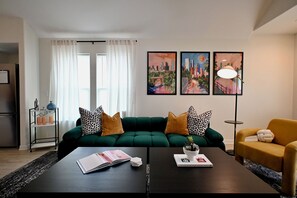 A modern living room with a green sofa, a yellow armchair, a coffee table with a book and a plant, and a cityscape painting on the wall. - Retro-Luxury 3BR/2BA Home-Minutes from Downtown and Houston hot spots (Houston)