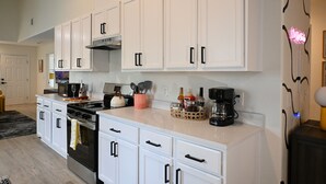 A modern kitchen with white cabinets, a stainless steel stove, and a coffee maker on the counter. - Retro-Luxury 3BR/2BA Home-Minutes from Downtown and Houston hot spots (Houston)