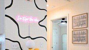 A hallway with a dark wooden cabinet, a neon sign, and two framed artworks on the wall. - Retro-Luxury 3BR/2BA Home-Minutes from Downtown and Houston hot spots (Houston)