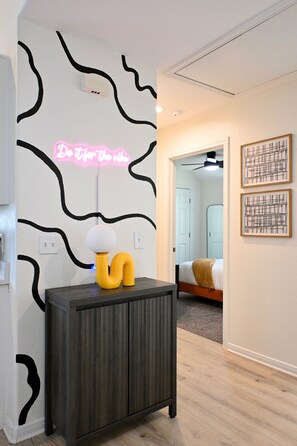 A hallway with a dark wooden cabinet, a neon sign, and two framed artworks on the wall. - Retro-Luxury 3BR/2BA Home-Minutes from Downtown and Houston hot spots (Houston)