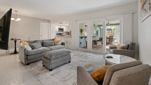 Ein modernes Wohnzimmer mit grauem Sofa, Ottomanen und Sesseln, einem Couchtisch und einem Flachbildfernseher.