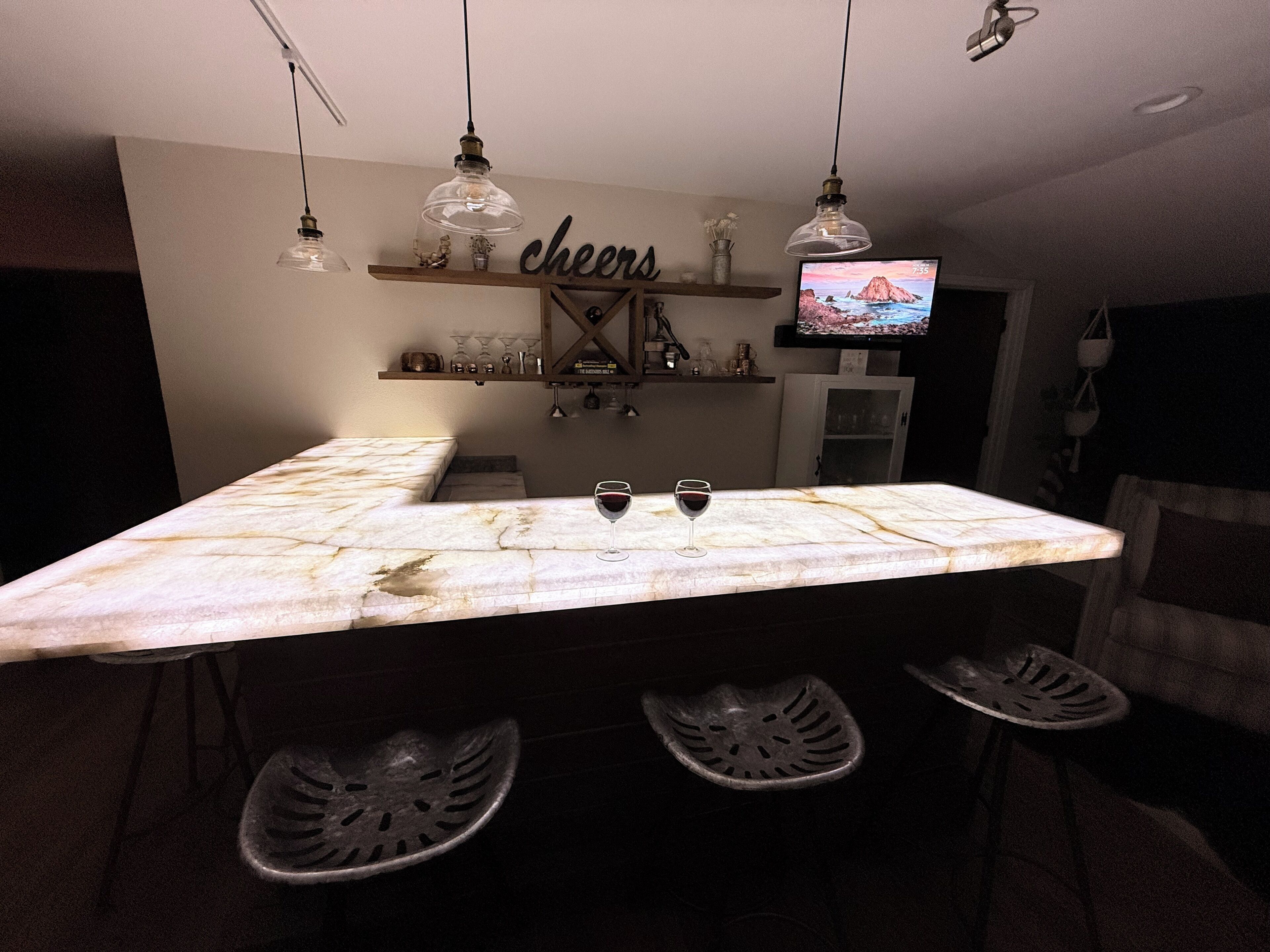 A dining area with a marble table, four chairs, a TV on the wall, and a shelf with decorative items.