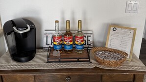 A coffee maker, three Torani syrup bottles, a framed welcome sign, and a basket of coffee pods on a wooden table. - Naci Vista Retreat - Incredible Lake Views (Bradley)