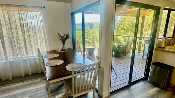 A dining area with a wooden table and chairs, a vase with flowers, and a view of a deck with outdoor furniture. - Naci Vista Retreat - Incredible Lake Views (Bradley)
