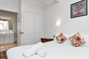 Un dormitorio con cama, dos almohadas, una mesita de noche, cómoda, espejo y puerta.