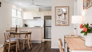 A modern kitchen with wooden cabinets, a dining table with chairs, a refrigerator, and a ceiling fan.