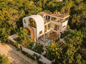 Une maison moderne à plusieurs étages, dotée d’une piscine et entourée d’une végétation luxuriante.