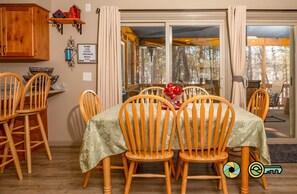 A dining area with wooden chairs and a table covered with a floral tablecloth. - Blue Bungalow | Private deck & fire pit (Basye)