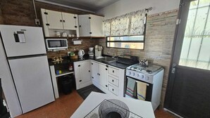 Une cuisine de taille réduite, avec des meubles blancs, un four à micro-ondes, une cuisinière à gaz et un réfrigérateur.