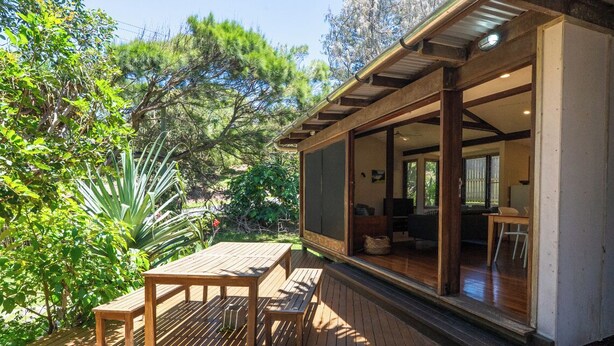 Una terraza de madera con una mesa y bancos, rodeada de abundante vegetación.