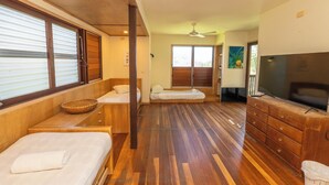 Una habitación con dos camas, televisión, ventilador de techo y un ventanal grande.