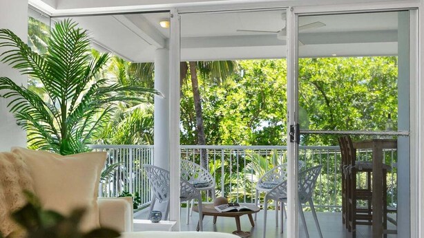 En balkon med udsigt over frodig vegetation, en hvid stol, et lille bord og en sofa med pude.