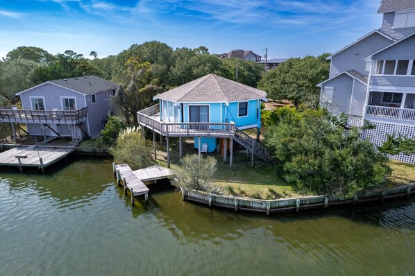 A house with a blue exterior, elevated on stilts over water, connected to a dock.