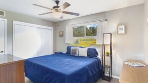 A bedroom with a bed, a ceiling fan, a window with a curtain, a bedside table, and a framed sign on the wall. - Cozy 1-bedroom condo in tranquil Osage Beach surrounded by all the Hot Spots!! (Osage Beach)