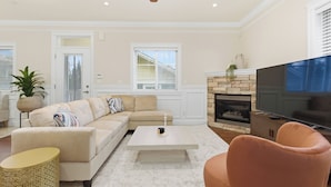 A living room with a beige sectional sofa, a coffee table, a pink armchair, a TV, and a fireplace.