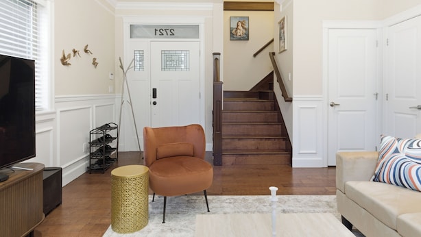 A living room with a television, a sofa, a chair, a staircase, and a door with a sign.