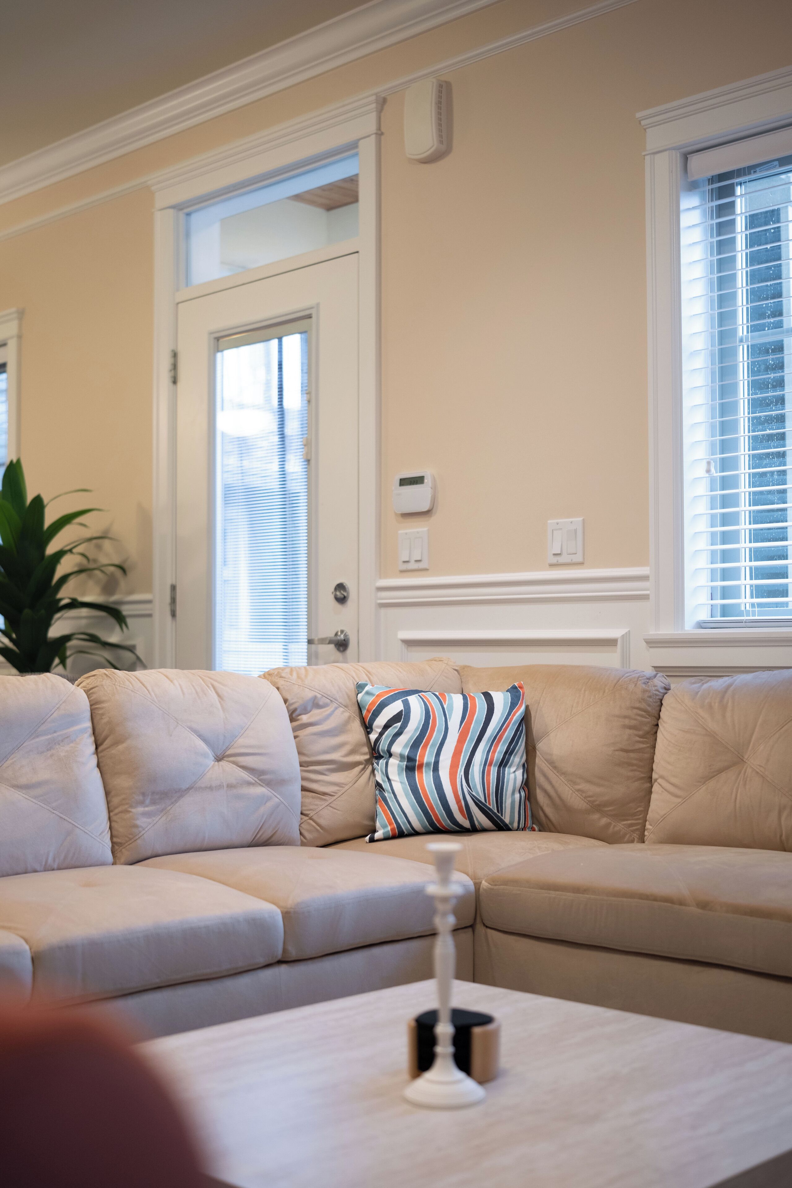Un salon aux tons beiges, avec un canapé beige, un coussin à rayures et une table blanche sur laquelle est posée une bougie.