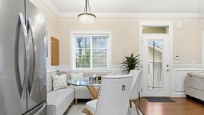 A modern kitchen with a stainless steel refrigerator, a dining table with chairs, and a window with blinds.
