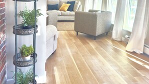 Ein Wohnzimmer mit Holzboden, einer Couch, einem Sessel und einem dekorativen Pflanzenstand.