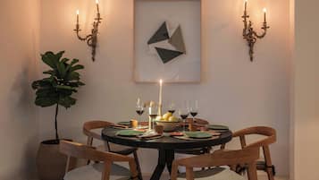 Un comedor con una mesa redonda, cuatro sillas de madera, una planta en maceta y candelabros fijos a la pared.