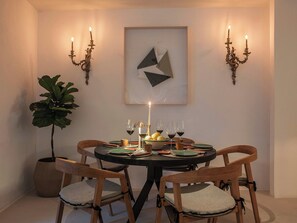 Zona pranzo con tavolo rotondo, quattro sedie di legno, una pianta in vaso e candelabri a parete.