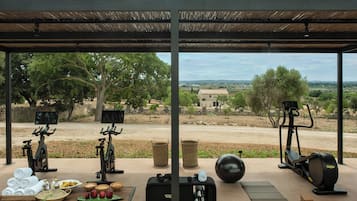 Un gimnasio al aire libre con equipo de ejercicio, una mesa con toallas y frutas, y vistas al campo.