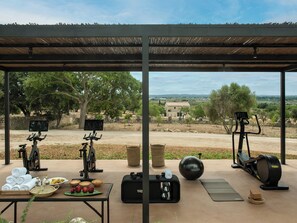 An outdoor gym with exercise equipment, a table with towels and fruits, and a view of the countryside. - The Lodge Mallorca (Sa Pobla)