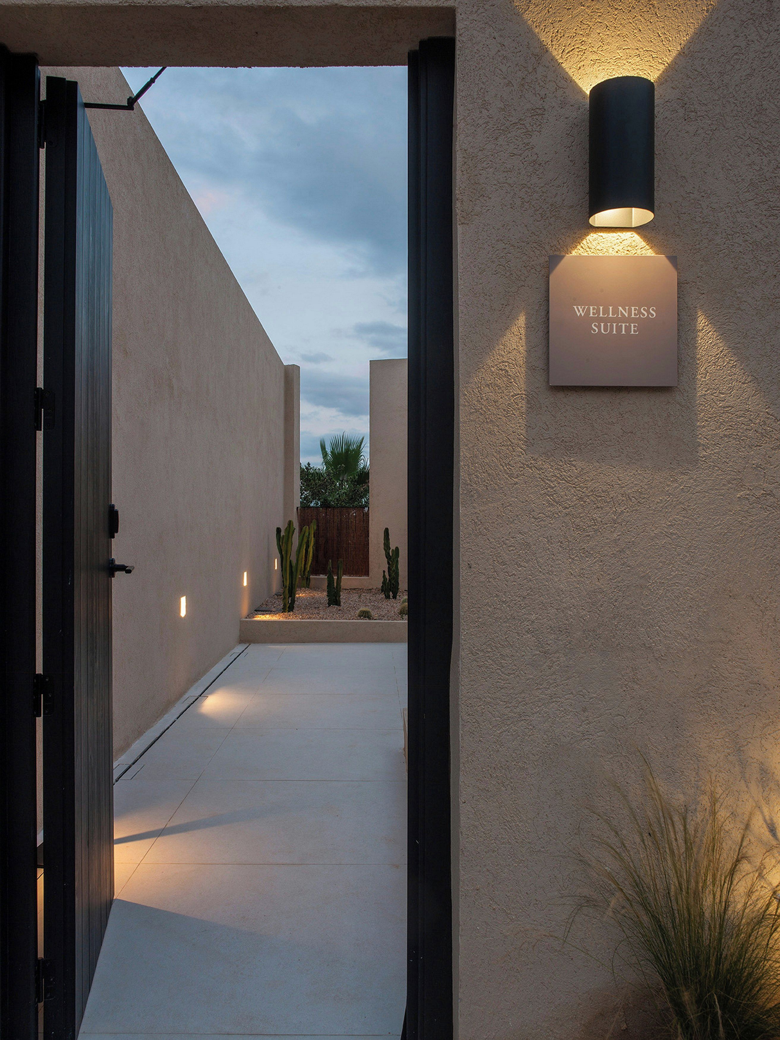 A pathway leading to a wellness suite with a sign, a cactus garden, and a textured wall.