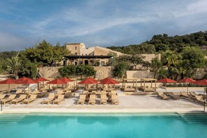 A poolside area with sun loungers and umbrellas, a clear pool, and a building with a stone facade in the background. - The Lodge Mallorca (Sa Pobla)