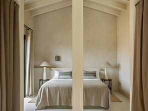 Une chambre à coucher comprenant un lit, deux lampes de chevet, une table de chevet, une lampe fixée au mur et une fenêtre avec des rideaux.