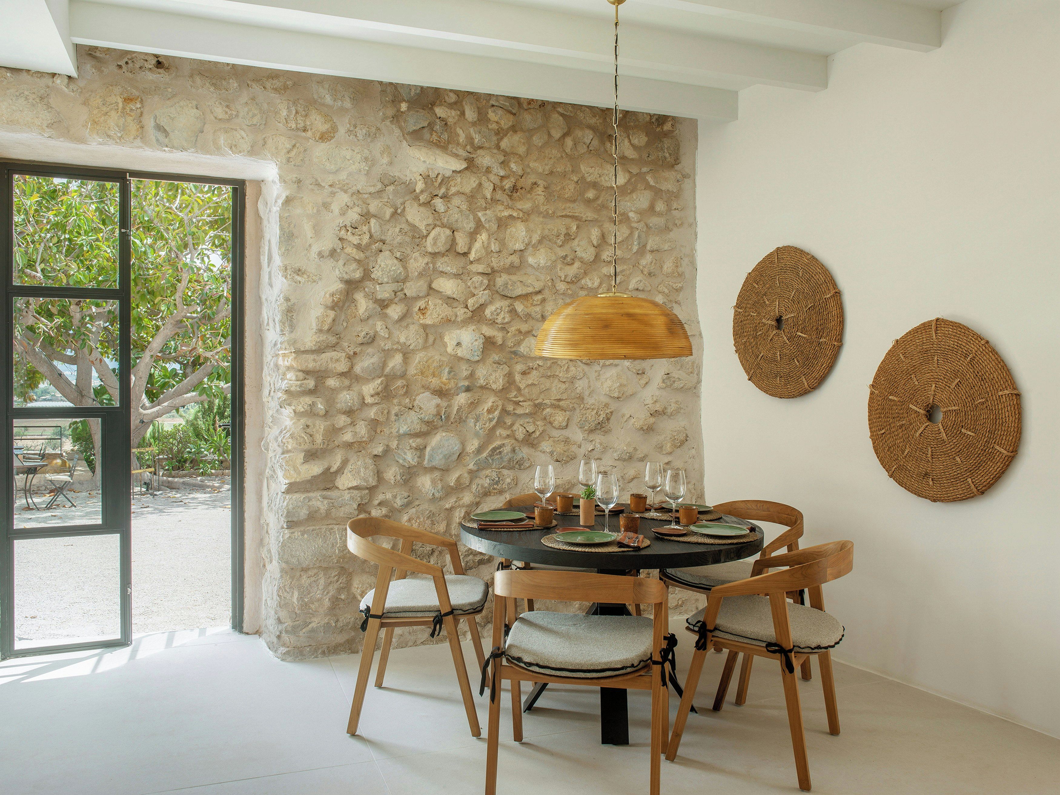 Un comedor con pared de piedra, sillas de madera, una mesa redonda y decoración mural tejida.