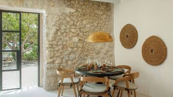 Un comedor con pared de piedra, sillas de madera, una mesa redonda y decoración mural tejida.