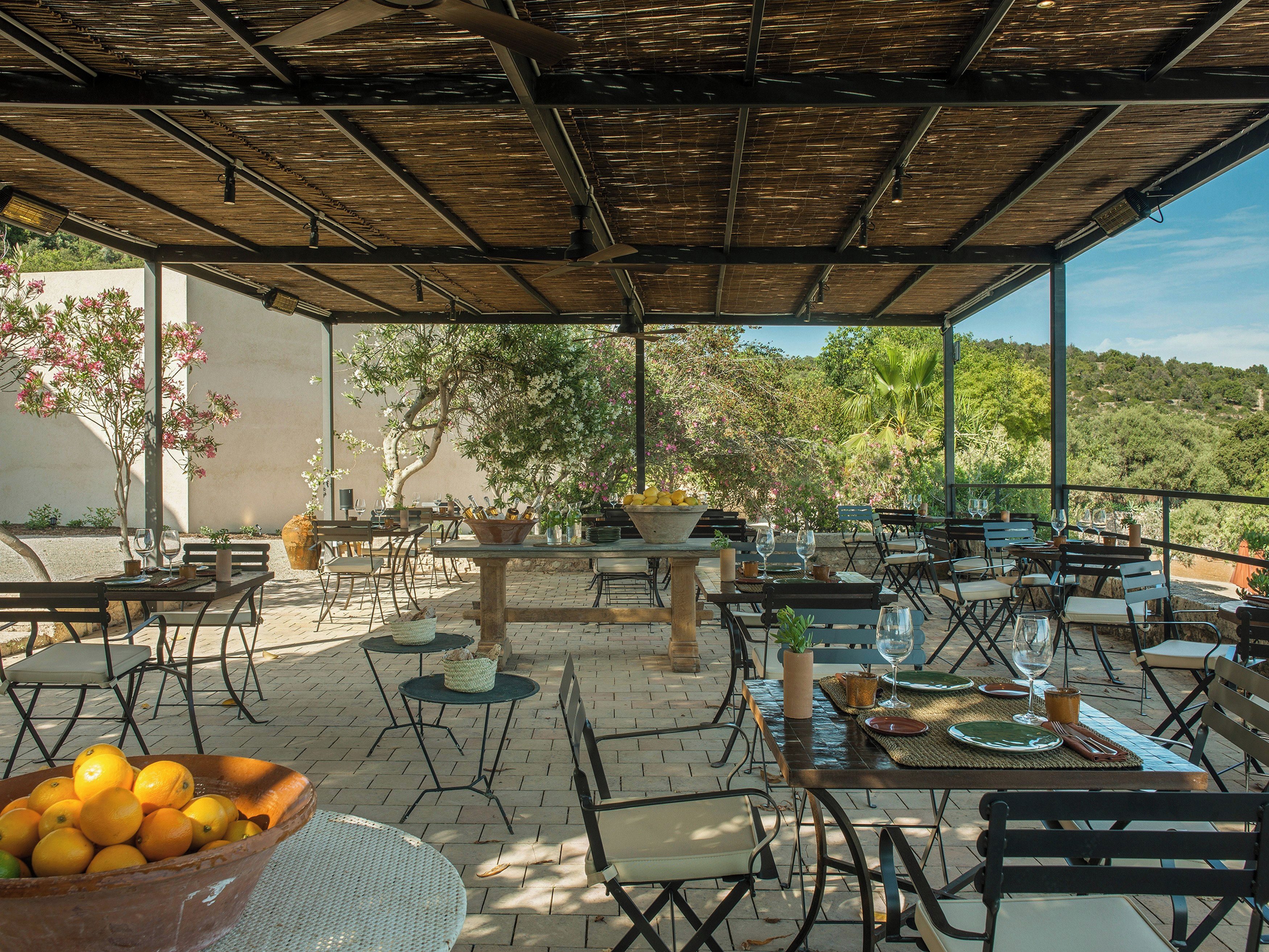 Un patio al aire libre con mesas y sillas, un bol de naranjas y vistas del paisaje circundante.