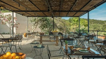 Un patio al aire libre con mesas y sillas, un bol de naranjas y vistas del paisaje circundante.