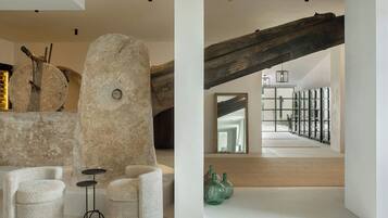A modern interior with a stone sculpture, a wooden beam, and a view of a staircase leading to a balcony.