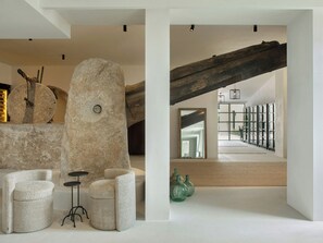 A modern interior with a stone sculpture, a wooden beam, and a view of a staircase leading to a balcony. - The Lodge Mallorca (Sa Pobla)