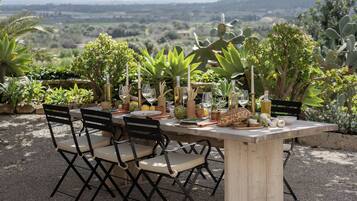 An outdoor dining table set up with chairs, surrounded by various plants and a scenic view in the background.