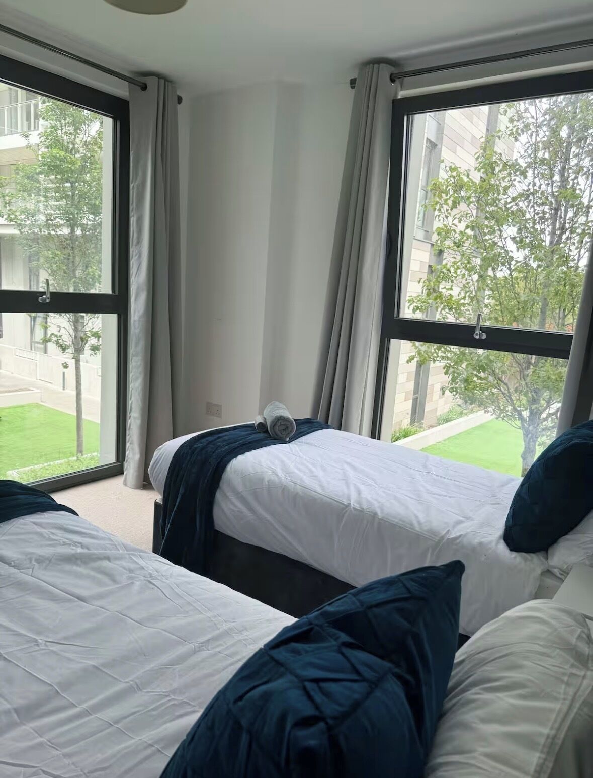 Una camera d'albergo con due letti, ampie finestre e vista su un prato verde e degli edifici.