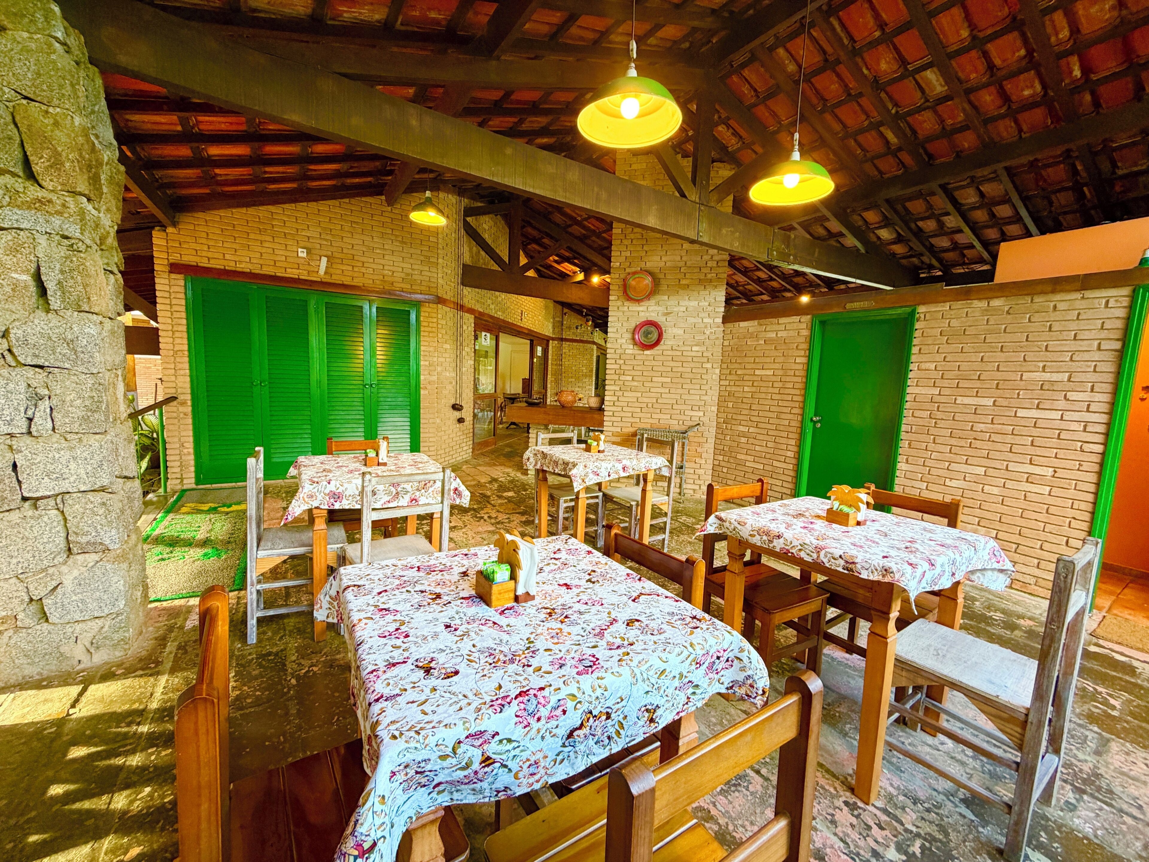 A rustic dining area with wooden tables and benches, green shutters, and exposed brick walls.