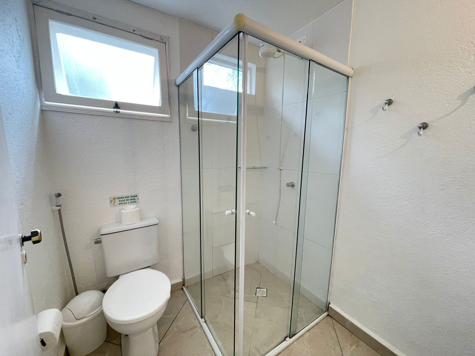 A bathroom with a glass shower enclosure, a toilet, and a window.