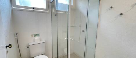 A bathroom with a glass shower enclosure, a toilet, and a window.