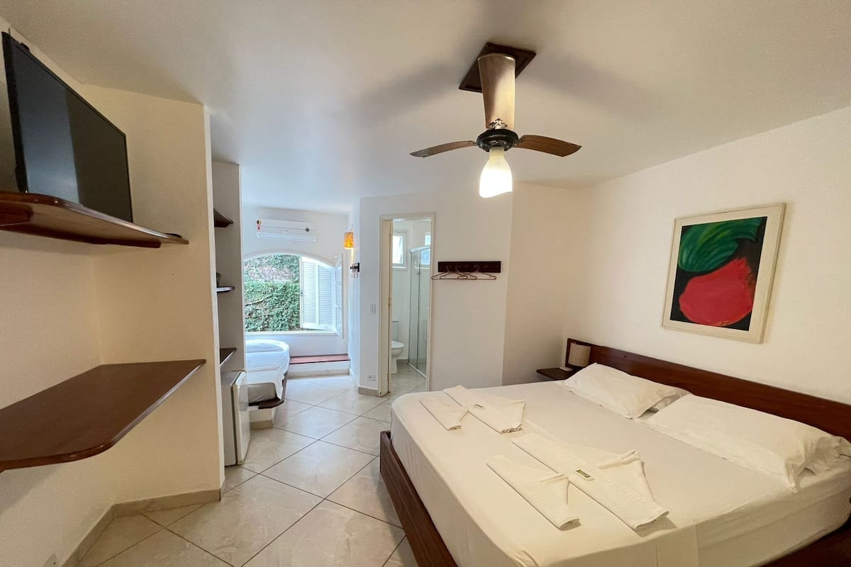 Une chambre d’hôtel avec un lit, un ventilateur de plafond, une salle de bain et une vue sur l’extérieur.