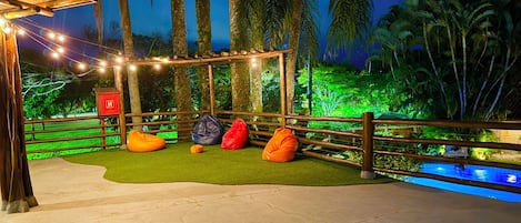 A nighttime outdoor seating area with string lights, a pool, and palm trees.