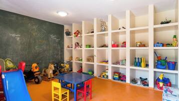 Uma sala de brincadeiras infantis com quadro negro, brinquedos e uma mesa.