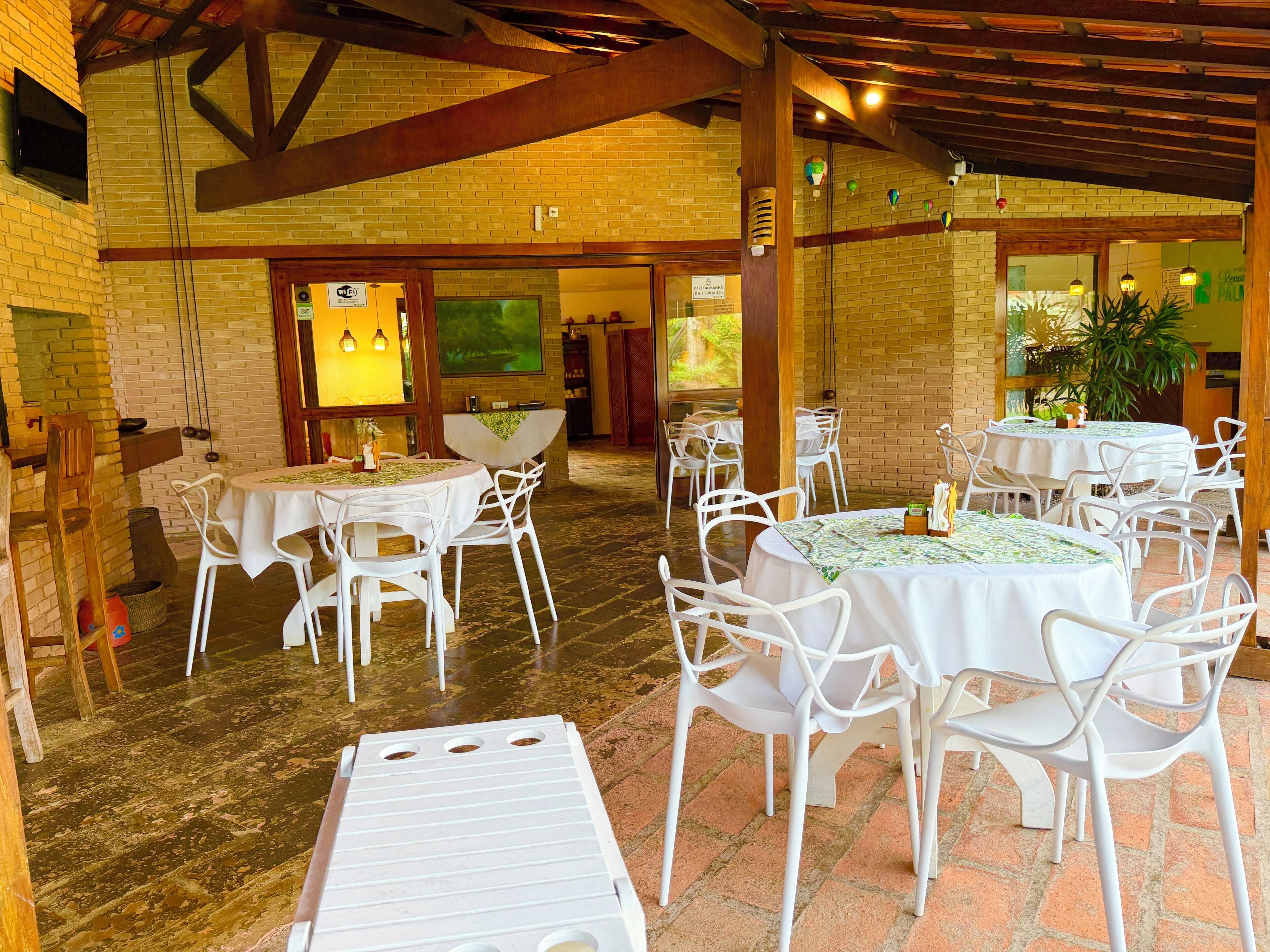 A restaurant with brick walls, white tables and chairs, and a wooden ceiling.
