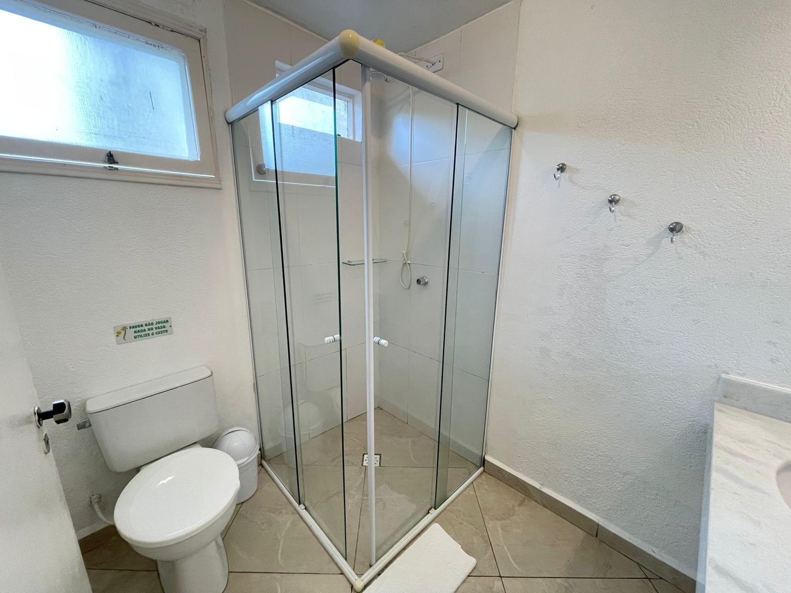 A bathroom with a glass shower enclosure, a toilet, and a window.