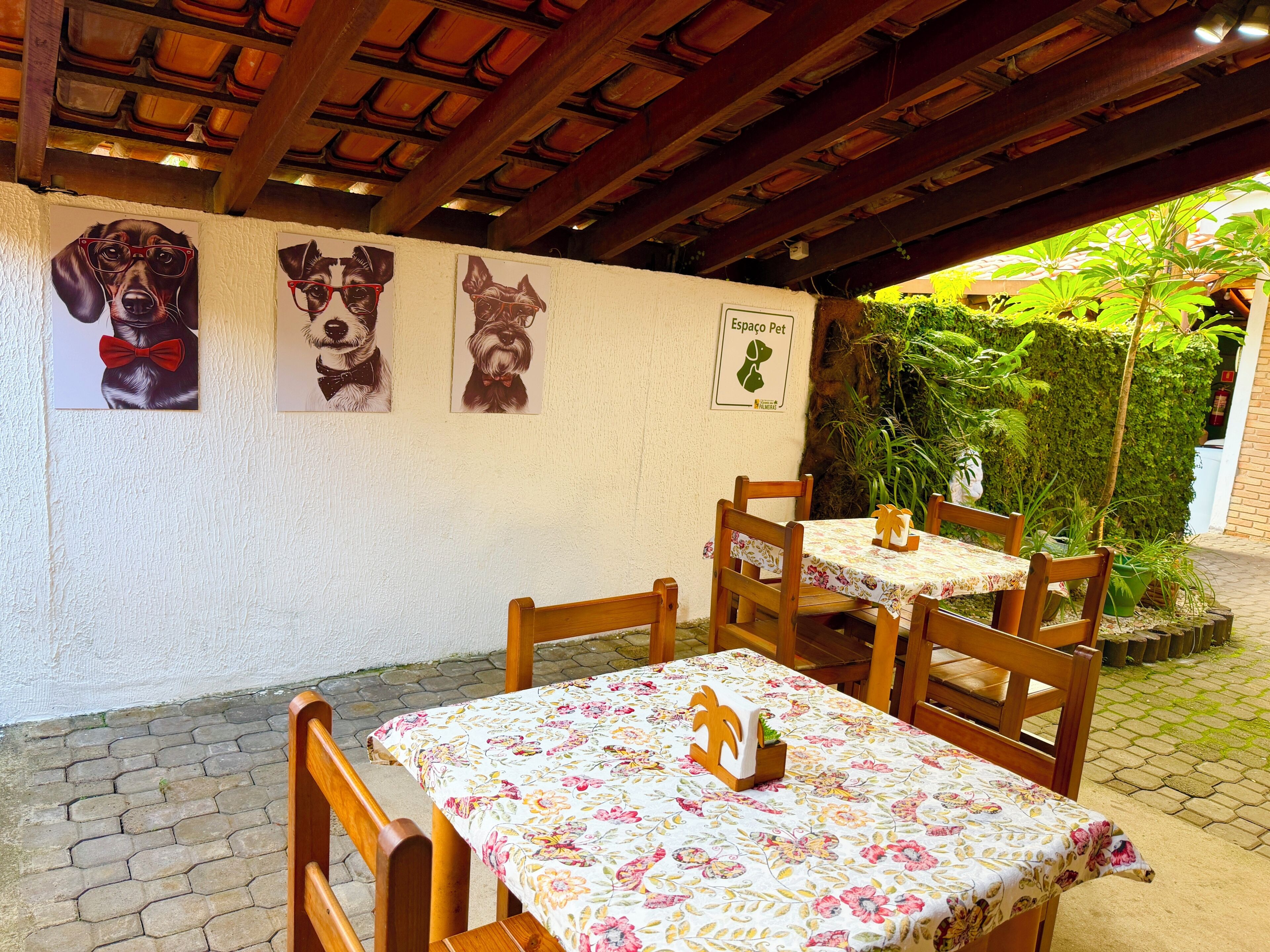 Un patio con mesas y sillas de madera, suelo de baldosas y una pared decorada con retratos de perros.
