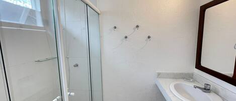 Un baño moderno con cabina de ducha de vidrio, lavamanos blanco y un espejo grande.
