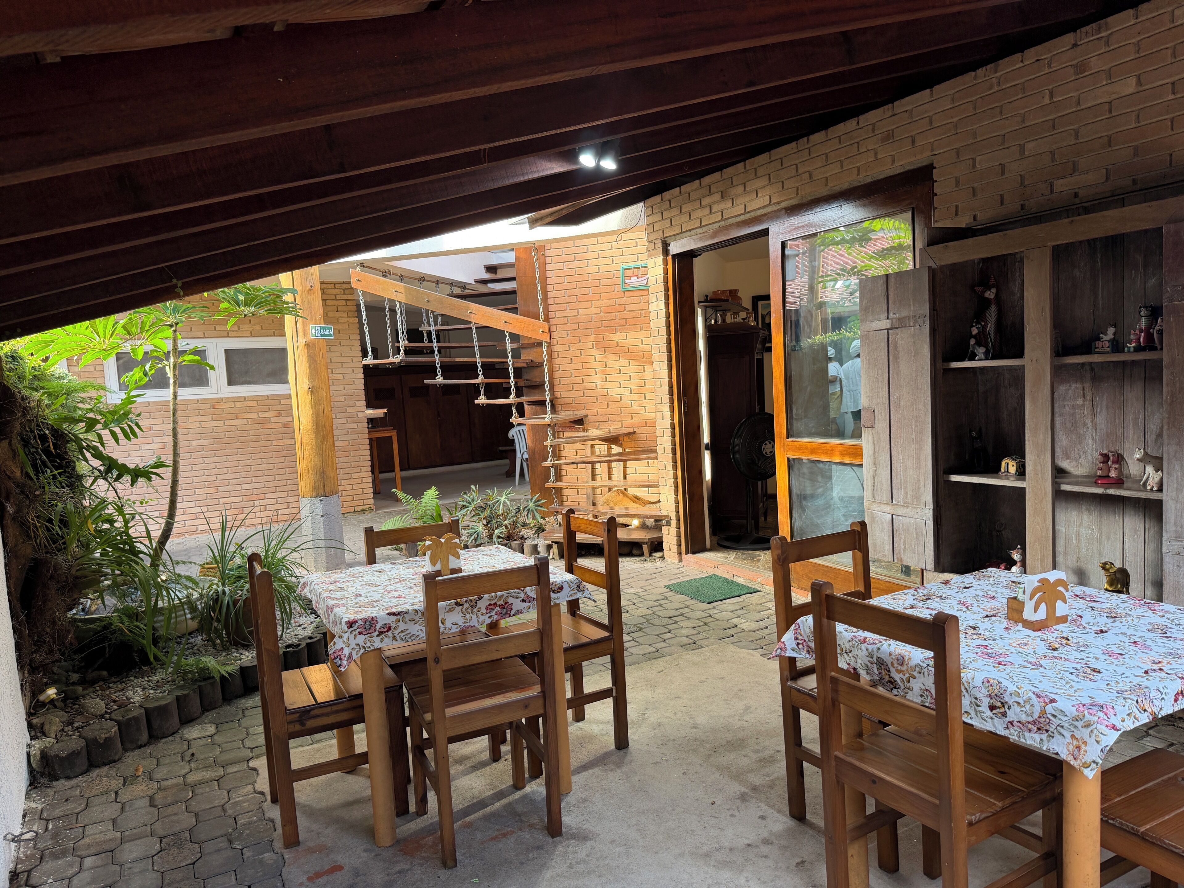 Un patio al aire libre con mesas y sillas de madera, un muro de ladrillo y un techo de madera.